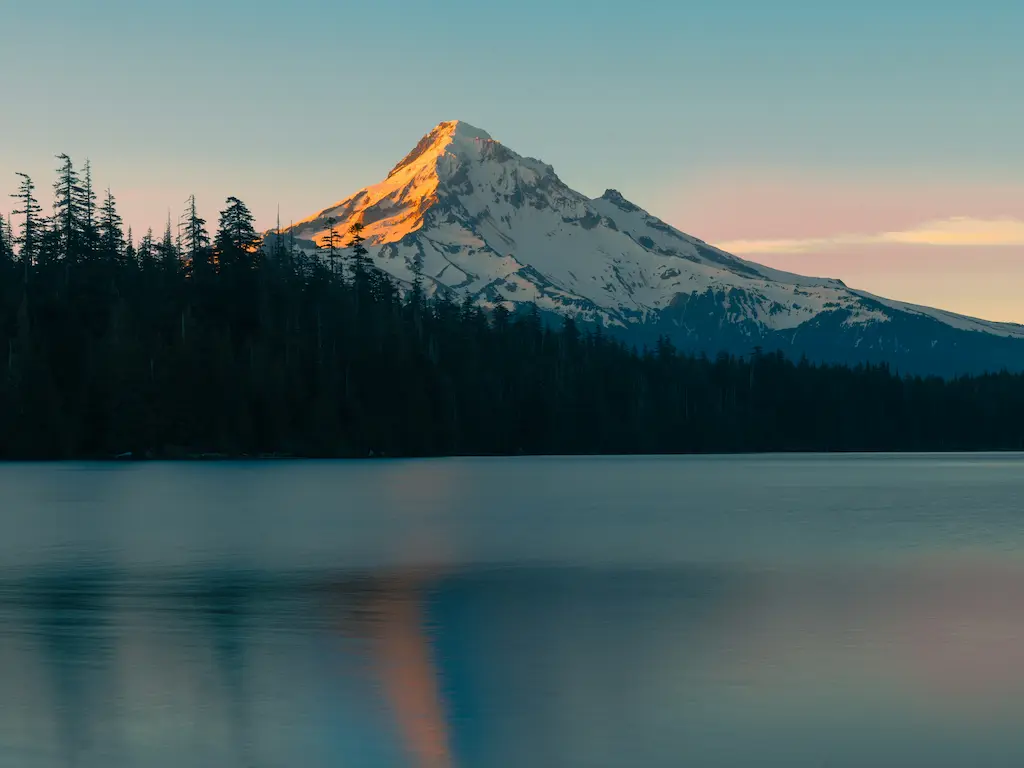 Alpenglow on one side of a mountain across from a lake
